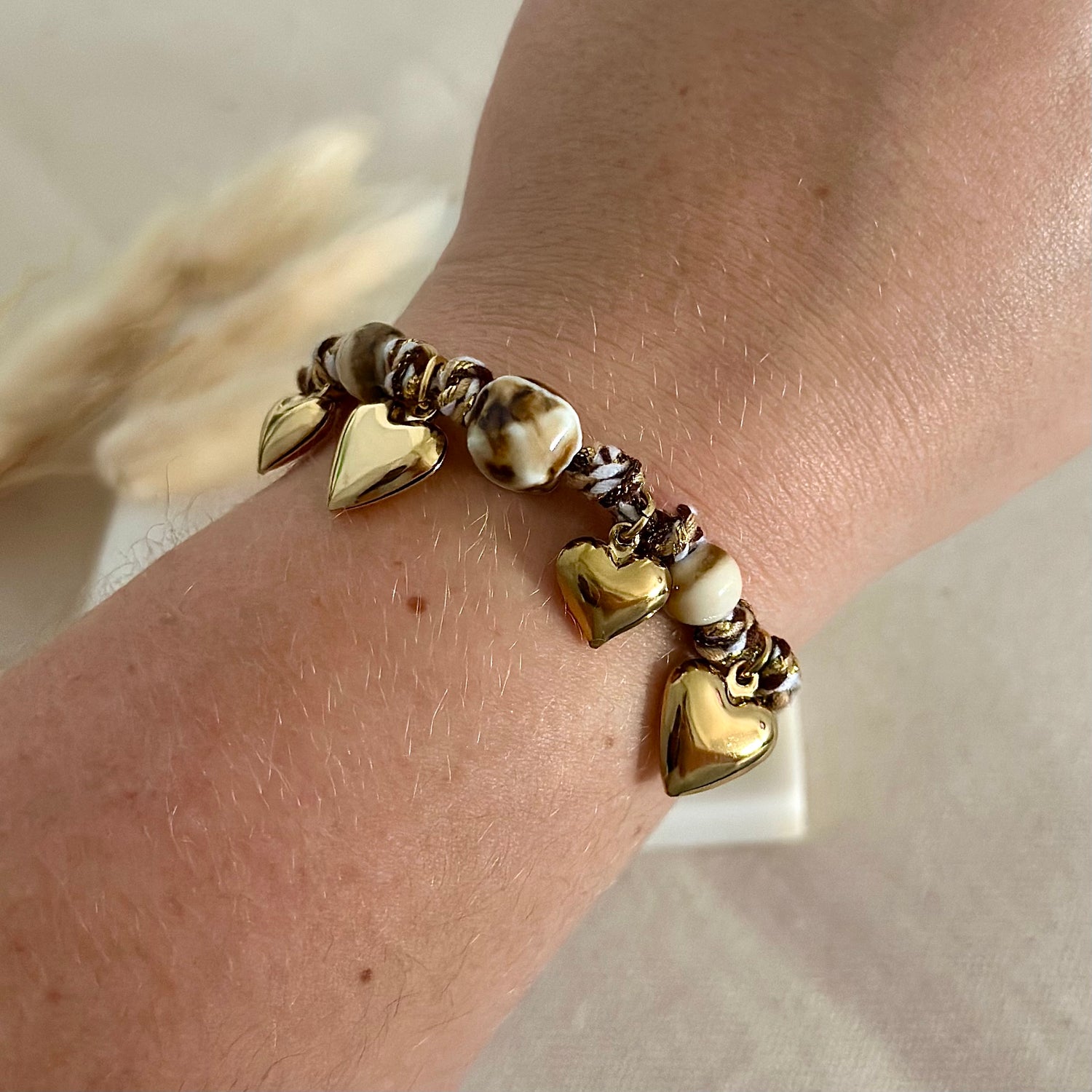 Bracelet doré porté en acier inoxydable pour femme tissu tressé marrons avec perles écailles de tortue et charms breloques coeurs dorés prise face - Zoela